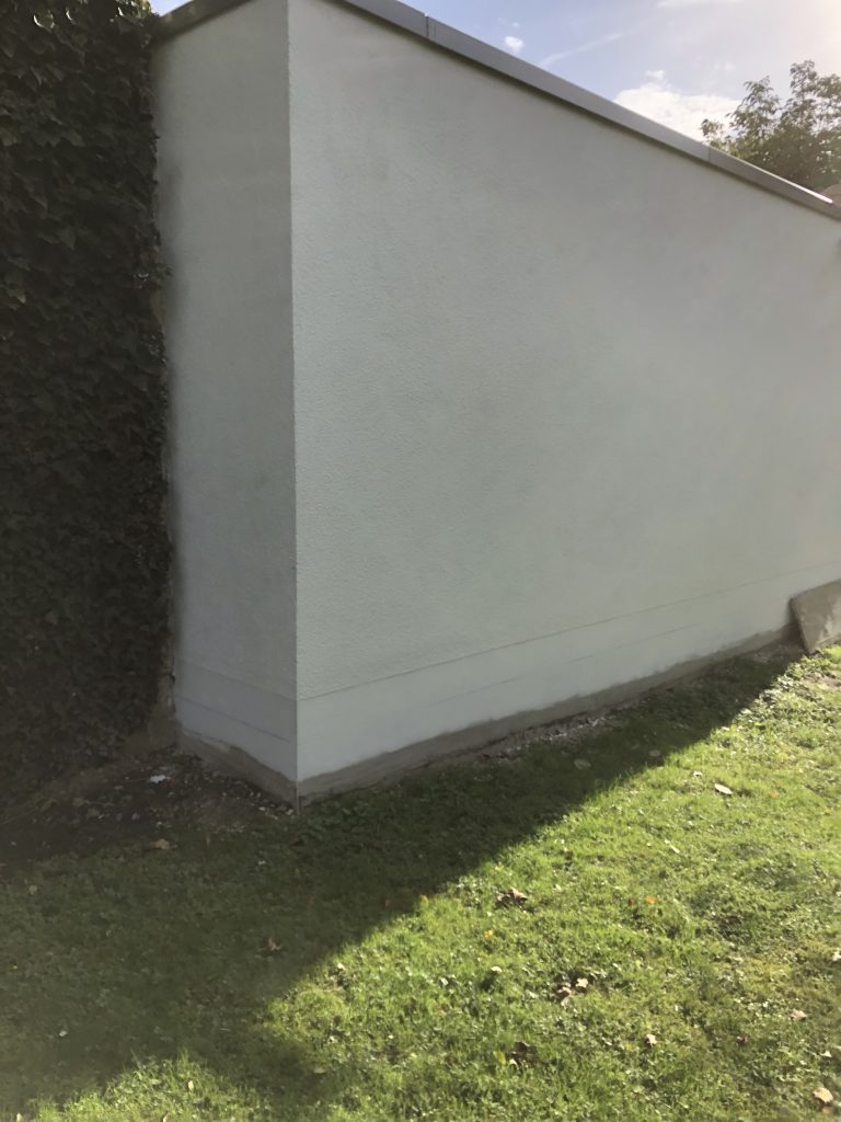 glatt verputzte Außenwand mit Sockelbereich in hellem Putz an einer Gartenmauer