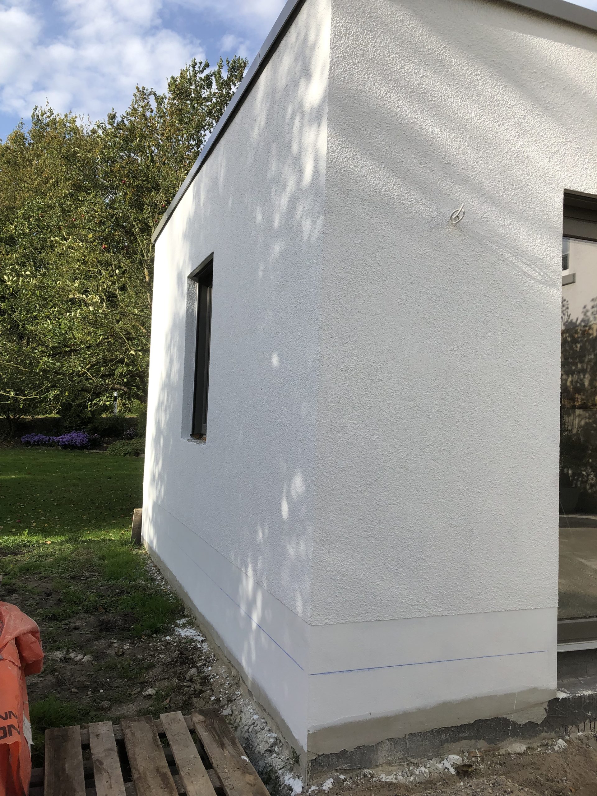 Wohnhausanbau mit fertiggestelltem hellen Fassadenputz und Sockelbereich