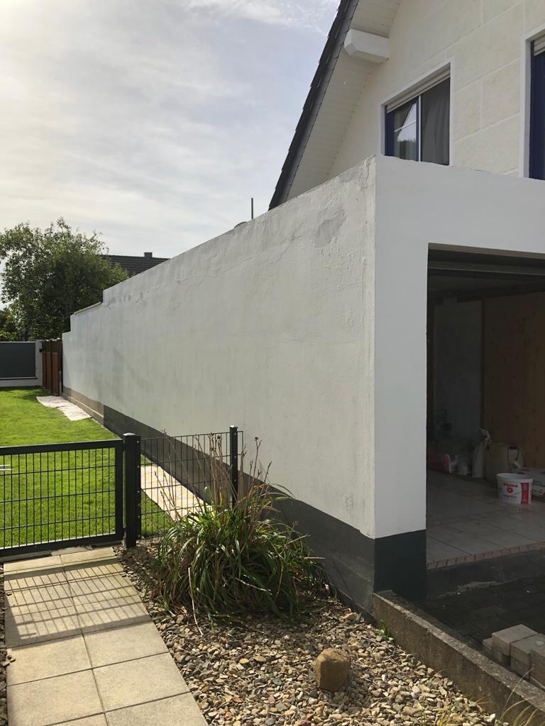 Lange Außenwand eines Wohnhausanbaus mit neu aufgetragenem Fassadenputz und dunklem Sockel